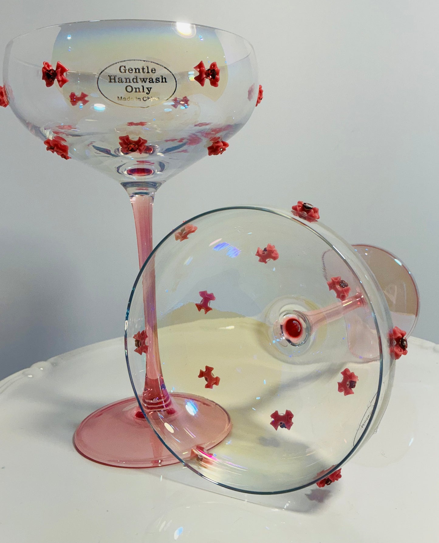 Set of 2 Iridescent pink coupe glasses feature a stem-to-base ombré effect decorated w/red bows 7”